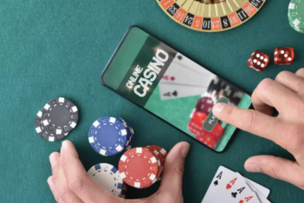 A képen egy online kaszinót játszó személy látható mobiltelefonján, poker zsetonokkal